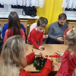 Dzieci z rodzicami wykonują wieńce bożonarodzeniowe.