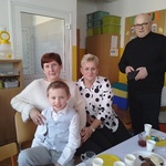 Chłopiec siedzi przy stole z babciami i dziadkiem.