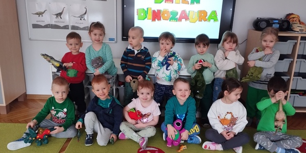Dzieci z zabawkowymi dinozaurami pozują do zdjęcia.